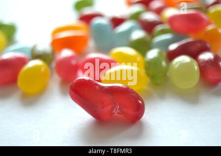 Verschiedene süße und saure Bunte Jelly Beans Bonbons mit verschiedenen Fruchtaromen, liegend auf einer weissen Fläche Stockfoto