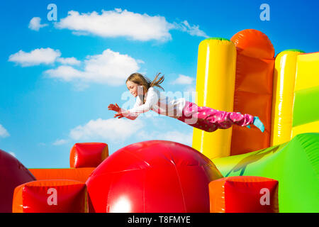 Gerne kleine Mädchen haben viel Spaß beim von Ball zu Ball springen auf ein Schloss aufpumpen. Stockfoto