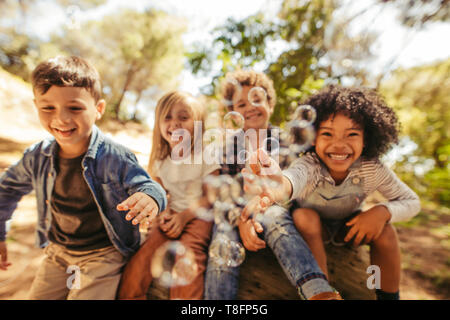 Gruppe von Kindern beim Spielen mit Seifenblasen im Freien. Freunde versuchen, die Blasen zu fangen. Stockfoto