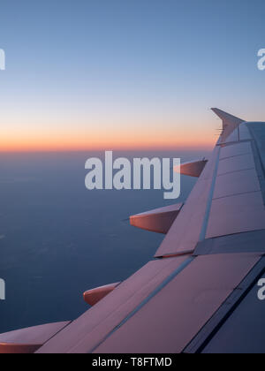 Seitenansicht der rechten Tragfläche eines Flugzeuges mit Orange Tönen von Sonnenaufgang Stockfoto