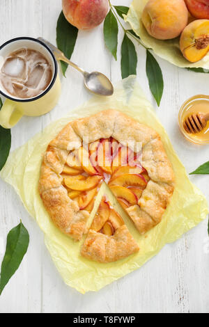 Pergament mit köstlichen Pfirsich Galette und Tasse erfrischenden Drink auf weiße Holztisch Stockfoto