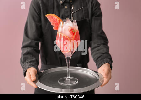 Kellnerin holding Metall Tablett mit frischen Grapefruit Cocktail in Glas auf farbigen Hintergrund Stockfoto