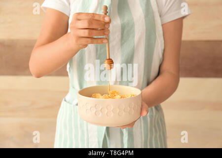 Frau gießen Honig auf gesunde Cornflakes auf hölzernen Hintergrund Stockfoto