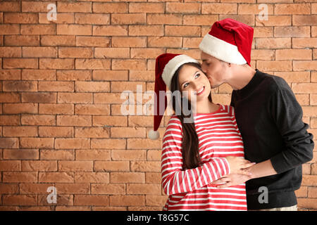 Portrait von netten jungen Paar in Santa Hüte gegen Mauer Stockfoto