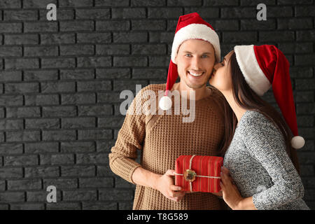 Junges Paar mit Weihnachtsgeschenk gegen dunkle Mauer Cute Stockfoto