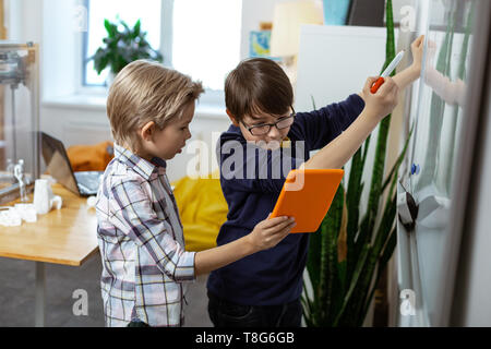 Blonde Junge mit orange tablet Während sein Freund Schreiben auf dem Schreibtisch Stockfoto