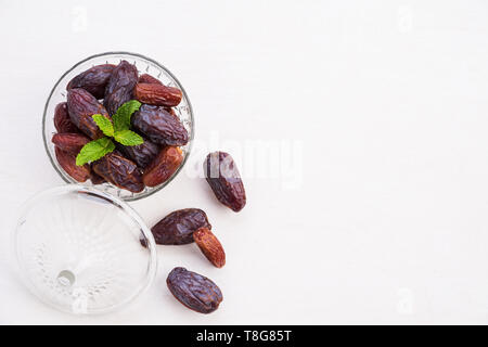 Ramadan Essen und Getränke Konzept. Termine Obst und grüne Minze in einer Schüssel auf einem weißen Tisch Hintergrund. Ansicht von oben, flach. Stockfoto