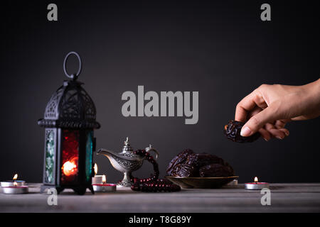 Ramadan Essen und Getränke Konzept. Frau Hand reicht, um eine Platte mit Datum mit Ramadan Laterne mit arabischen Lampe, Holz Rosenkranz, Tee, Obst und Termine Stockfoto