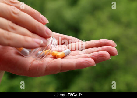 Frau mit Pillen, weibliche Hände mit einer Flasche Tabletten in Kapseln auf verschwommenes grün Natur Hintergrund. Konzept der Vitamine für die Schönheit, Diet Pill Stockfoto