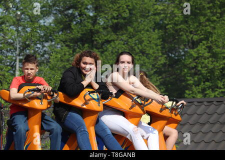 Moskau, Russland - Mai 2019: die Leute haben Spaß auf Fahrten in einem Vergnügungspark. Glückliche Mädchen und junge sitzt auf einem Karussell in Sokolniki Park, Familie Freizeit Stockfoto