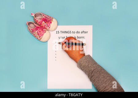 Bildunterschrift 15 Dinge zu erledigen, nachdem dein Baby ist geboren. Weiße A4-Blatt auf einem blauen Hintergrund neben Baby Pink booties Stockfoto