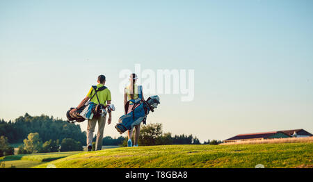 Glückliches Paar mit Ständer Taschen in Richtung Golfplatz an einem sonnigen Tag Stockfoto