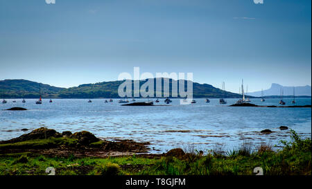 Yachten im Loch nan Ceall aus dem Dorf Arisaig an der Westküste von Schottland verankert mit dem markanten Umriss der Insel Eigg im b Stockfoto