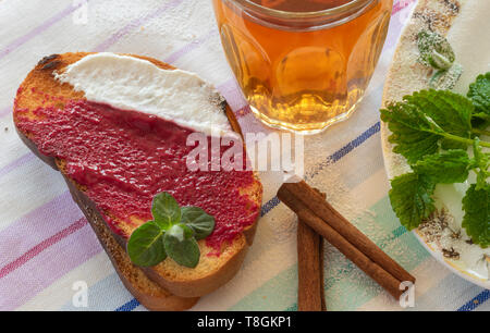 Zwei Toast mit Himbeere Maische und Joghurt, Glas Tee, Zimt und Minze. Stockfoto