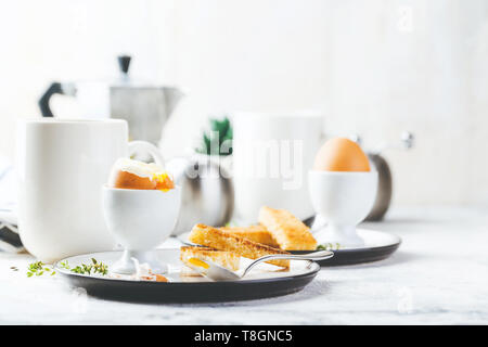 Weich gekochte Eier zum Frühstück mit Toast und Kaffee Tasse im Hintergrund Stockfoto