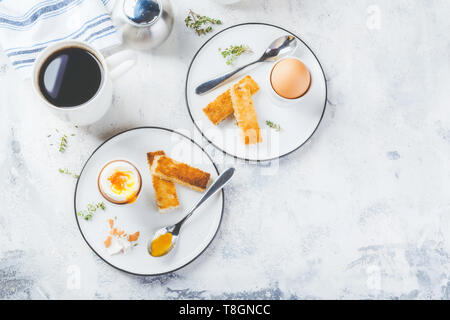Weich gekochte Eier zum Frühstück mit Toast und Kaffee Tasse im Hintergrund. Platz für Text. Ansicht von oben. Stockfoto