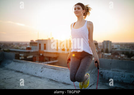 Porträt der jungen Frau mit Seil springen auf der Dachterrasse. Fitness Frauen tun überspringen Training im Freien an einem sonnigen Tag. Stockfoto