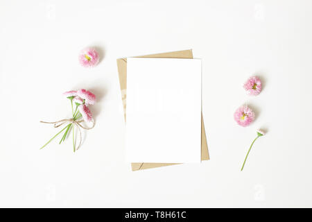 Feminine Schreibwaren, desktop Mock-up-Szene. Vertikale leere Grußkarte, craft-Umschlag und Daisy Bouquet und Blumen auf weißem isoliert Stockfoto