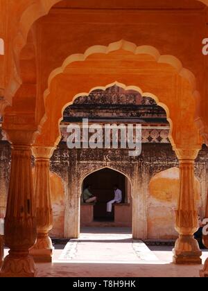 Blick durch bernsteinfarbene Bögen von zwei jungen Männern sitzen reden in einer kühlen Ecke des Amber Palace in Jaipur "The Pink City", Rajasthan, Indien Stockfoto