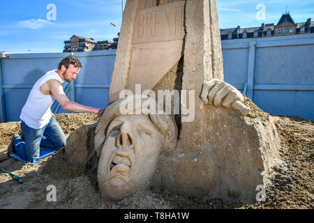 Sand Skulptur Künstler Johannes Hogebrink arbeitet an einem Brexit themed Skulptur an der Weston Sandskulpturenfestival, Weston-super-Mare, mit Premierminister Theresa kann ihren eigenen Kopf abschneiden über eine Guillotine. Stockfoto