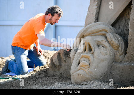 Sand Skulptur Künstler Johannes Hogebrink arbeitet an einem Brexit themed Skulptur an der Weston Sandskulpturenfestival, Weston-super-Mare, mit Premierminister Theresa kann ihren eigenen Kopf abschneiden über eine Guillotine. Stockfoto