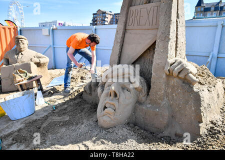 Sand Skulptur Künstler Johannes Hogebrink arbeitet an einem Brexit themed Skulptur an der Weston Sandskulpturenfestival, Weston-super-Mare, mit Premierminister Theresa kann ihren eigenen Kopf abschneiden über eine Guillotine. Stockfoto