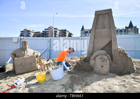 Sand Skulptur Künstler Johannes Hogebrink arbeitet an einem Brexit themed Skulptur an der Weston Sandskulpturenfestival, Weston-super-Mare. Die Skulptur mit Premierminister Theresa kann ihren eigenen Kopf weg schneiden mit einer Guillotine während US-Präsident Donald Trump Uhren auf. Stockfoto