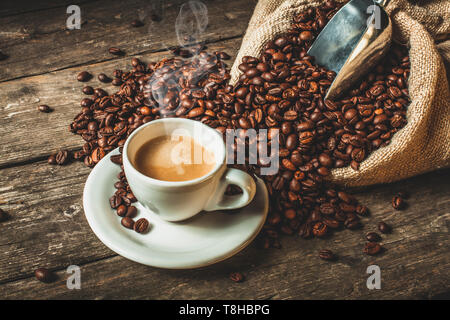 Dampfenden Kaffee in traditionellen Keramik Schale, Jute Sack mit gerösteten Bohnen auf hölzernen Tisch. Stockfoto