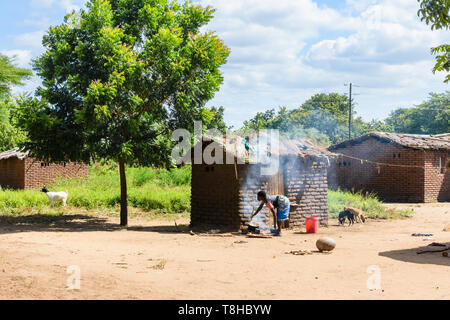 Malawische Frau steht Kochen mit einem Topf auf einem offenen Feuer in einem Dorf in Malawi Chikwawa außerhalb eines Gras überdachte Schlamm Gebäude, wie Ihre Küche serviert Stockfoto