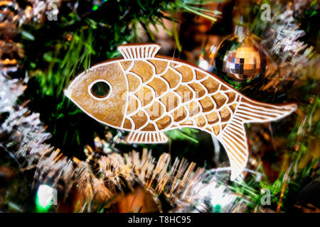Süßen Lebkuchen in Fisch hängen an reich geschmückten Weihnachtsbaum. Handgefertigte aromatische Cookie closeup auf unscharfen Hintergrund der grünen Nadeln. Weihnachten Girlanden. Stockfoto