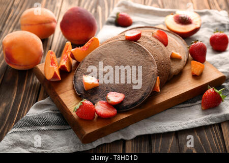 Leckere Schokolade Pfannkuchen mit Erdbeeren in Scheiben geschnitten und Pfirsich auf Holzbrett Stockfoto