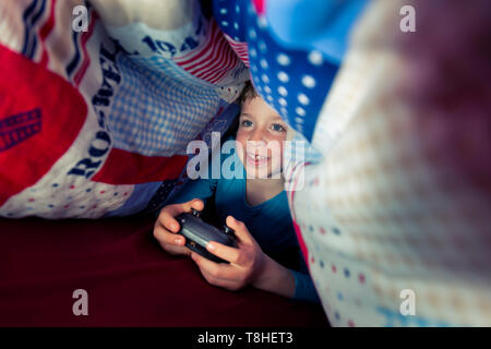 Junge, 8 Jahre, sectretly spielen, computer spiel im Bett Stockfoto