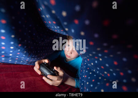 Junge, 8 Jahre, sectretly spielen, computer spiel im Bett Stockfoto