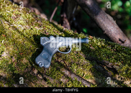 Spielzeugpistole aus Blei liegt auf einem alten Baum mit Moos. Stockfoto