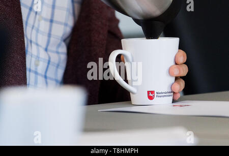 Hannover, Deutschland. 13. Mai, 2019. Ein Journalist gießt Kaffee in eine Tasse mit der Aufschrift "Niedersächsisches Finanzministerium' (Ministerium der Finanzen des Landes Niedersachsen) während einer Präsentation der regionalisierten Ergebnisse der steuerlichen Schätzung für Niedersachsen. Credit: Julian Stratenschulte/dpa/Alamy leben Nachrichten Stockfoto