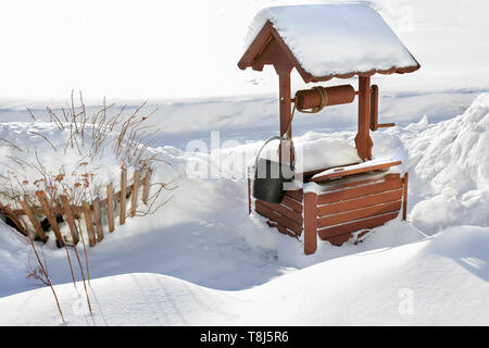 Holz- Jahrgang gut mit Wasser im Schnee. Winterlandschaft des russischen Hinterland. Ein altes Gerät zur Entnahme von Wasser. Stockfoto