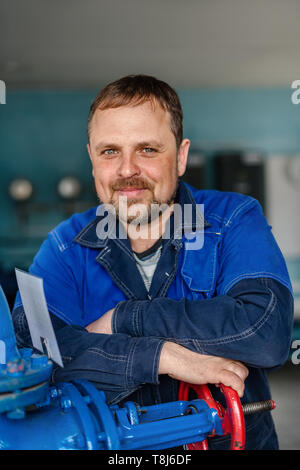 Porträt eines Schlossers im Kesselraum am Arbeitsplatz. Ein weißer Mann mit einem Bart mit freundlichen Augen sieht in die Kamera lächelt. Stockfoto