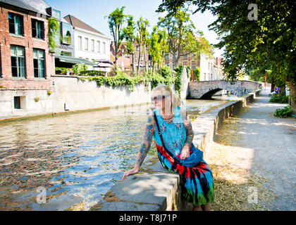 Frau, die allein auf einer niedrigen Wand am Ufer des Kanals sitzt, die die Aussicht genießen kann.Brügge, Belgien. Stockfoto