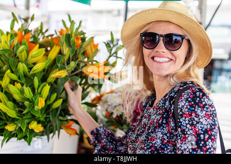 Blond mediterrane Frau, Sonnenbrille und Hut Blumen berühren am Markt Stockfoto