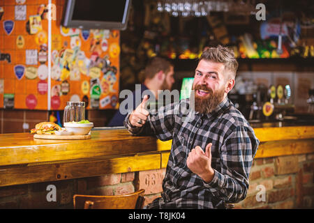 Kalorienreiche Snacks. Hipster entspannen im Pub. Pub ist ein entspannender Ort Drink zu entspannen. Brutale hipster bärtigen Mann an der Theke sitzen. Mann mit Bart Bier trinken essen burger Menü. Essen im Pub. Stockfoto