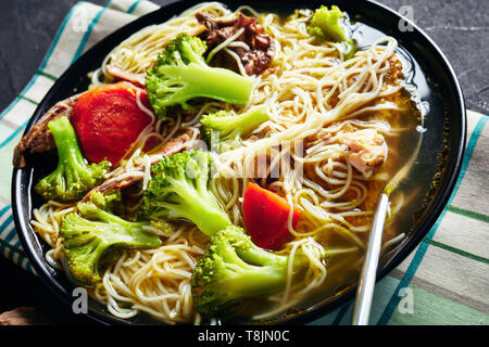 Langsam gekochtes Huhn Nudelsuppe mit Brokkoli, Karotten und Gewürze in einem schwarzen Schüssel auf eine konkrete Küche Tabelle, Ansicht von oben, close-up Stockfoto