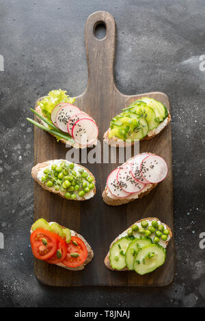 Verschiedene veganen Sandwiches mit Gemüse, Rettich, Sellerie, Tomate, Roggenbrot auf Schwarz. Top vew. Appetizer für Party. Flach. Stockfoto