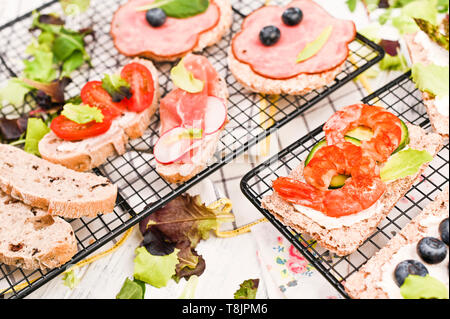 Verschiedene Sandwiches zum Frühstück auf einem weißen Holz- Hintergrund. Cracker mit Garnelen, Gemüse, Käse und Schinken Stockfoto