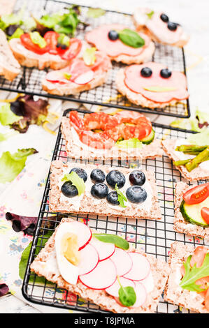 Verschiedene Sandwiches zum Frühstück auf einem weißen Holz- Hintergrund. Cracker mit Garnelen, Gemüse, Käse und Schinken Stockfoto