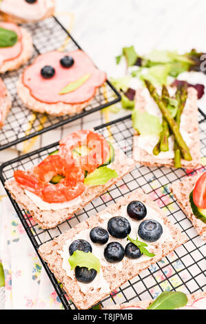 Verschiedene Sandwiches zum Frühstück auf einem weißen Holz- Hintergrund. Cracker mit Garnelen, Gemüse, Käse und Schinken Stockfoto