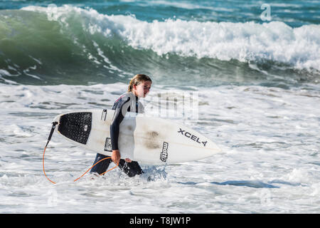 Eine junge müde weibliche surfer Ihr Surfbrett tragen und zu Fuß aus dem Meer auf den Fistral in Newquay in Cornwall. Stockfoto