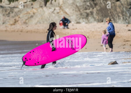 Eine müde weibliche Surfer mit einem bunten Surfboard und zu Fuß aus dem Meer auf den Fistral in Newquay in Cornwall. Stockfoto