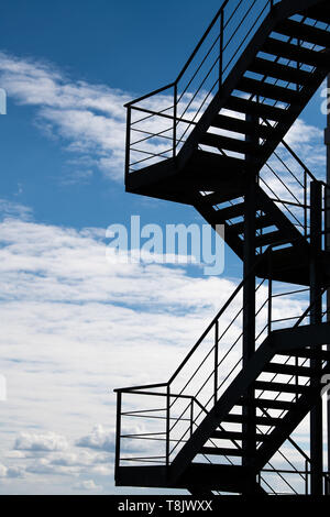 Treppe in den Himmel - ein Feuer entkommen oder eine externe Treppe auf ein Gebäude gegen einen hellen Wolkenhimmel Silhouette Stockfoto