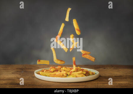 Bratkartoffeln mit Ketchup fliegen auf einer Keramikplatte auf einem alten Holztisch Stockfoto