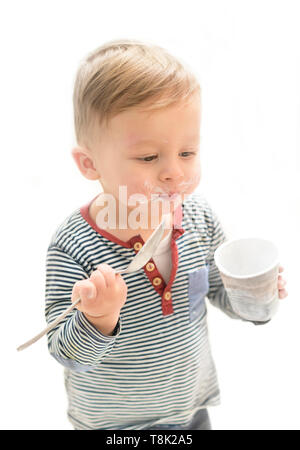 Little Boy essen Joghurt mit starken Appetit, in eine lustige unordentlich Gesicht Stockfoto